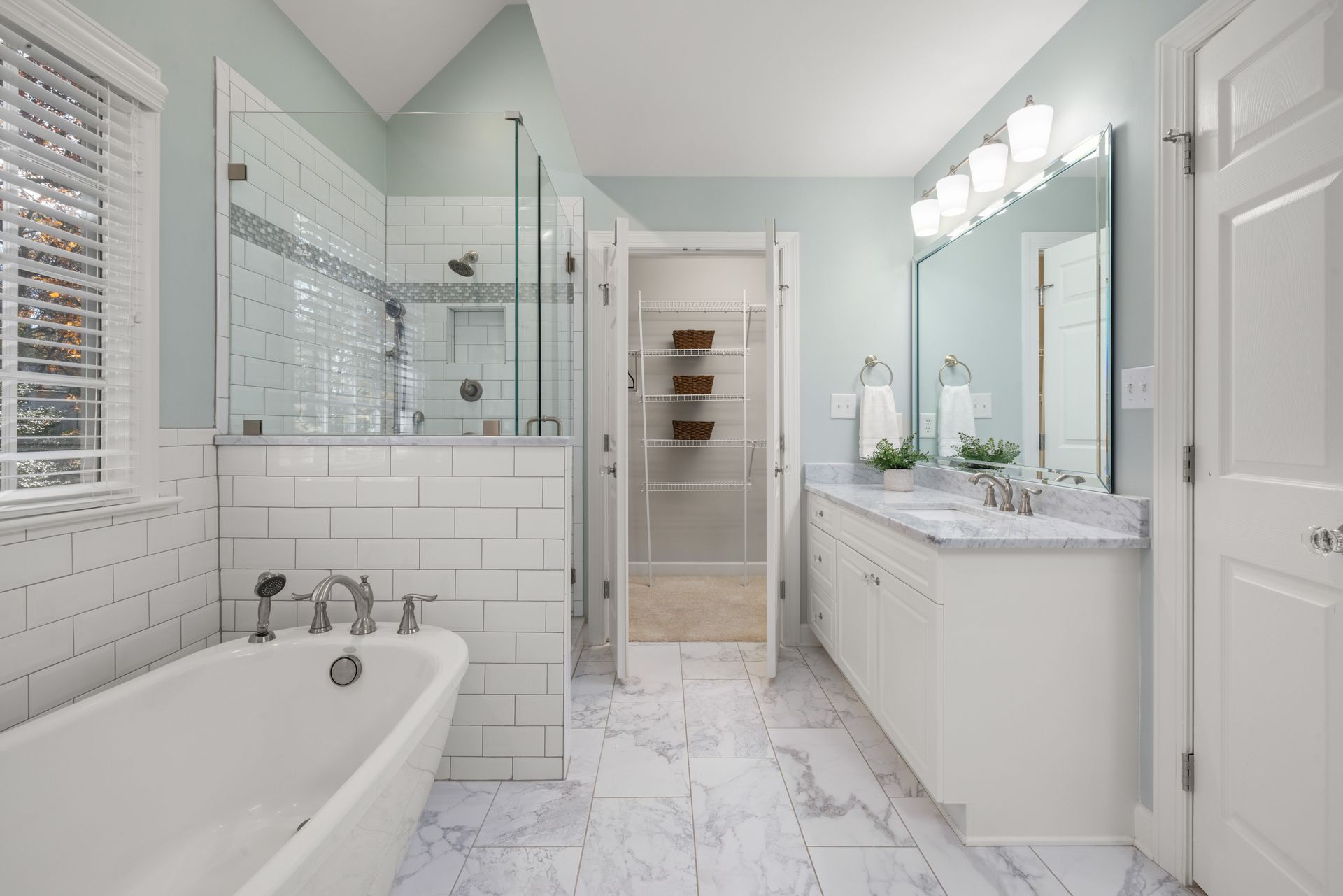 Bright white bathroom with tub, glass shower, vanity, and marble-style tile floors