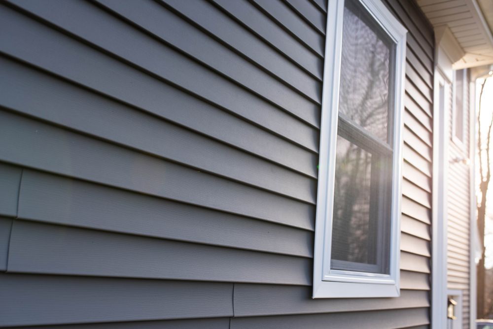 Gray house siding with a white-trimmed window and front door beside a sunlit porch