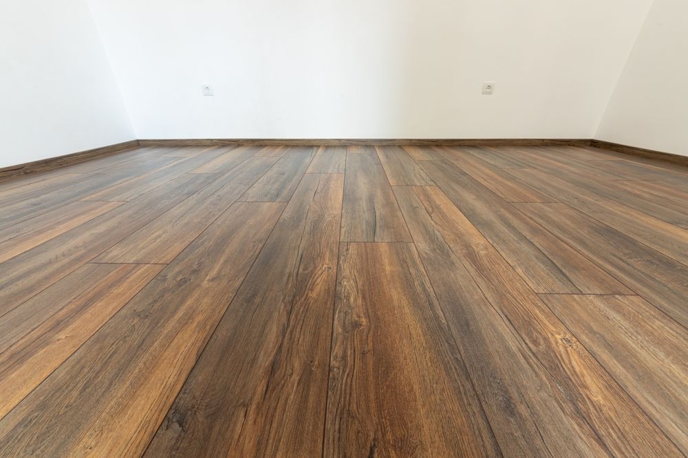 Empty room with wood-look flooring and white walls, viewed from a low angle.