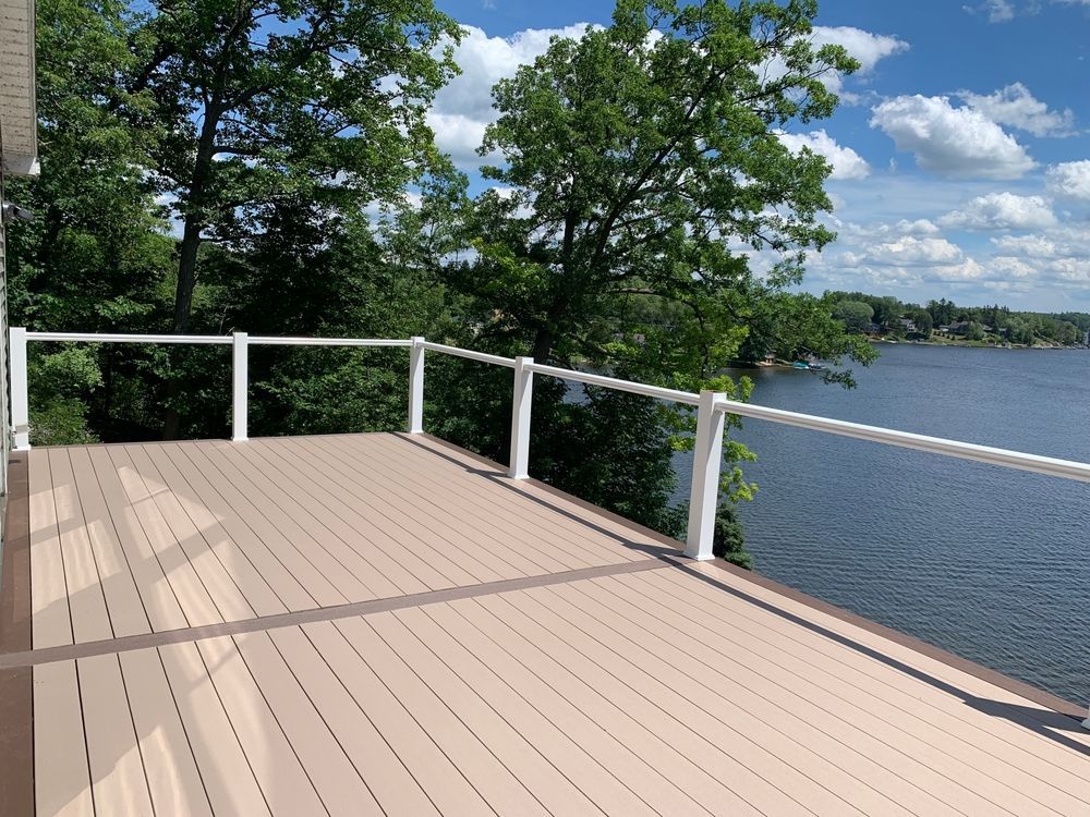Wooden deck overlooking a calm lake, with white railings and green trees under a blue sky.