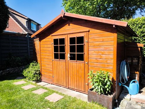 Wooden garden shed with double doors, next to lawn and potted plants in a sunny backyard