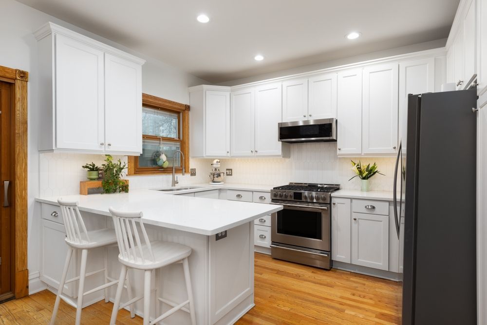 Bright white kitchen with island, bar stools, stainless appliances, and wood floors