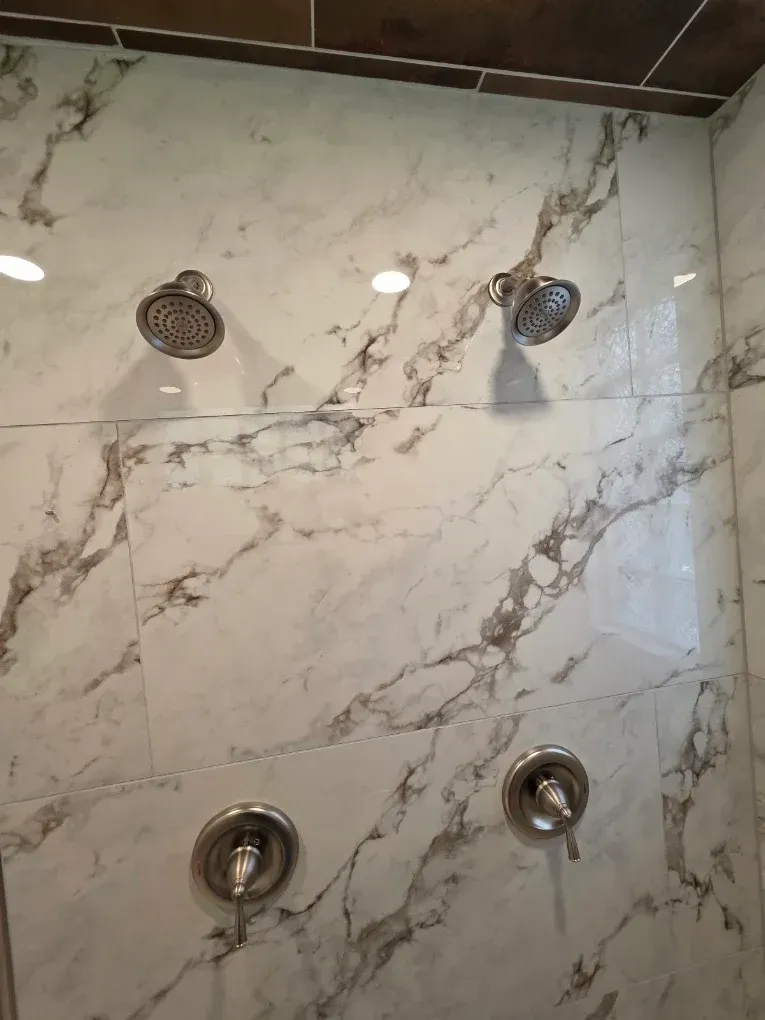 Shower wall with marble-look tiles and four chrome shower fixtures, including two showerheads