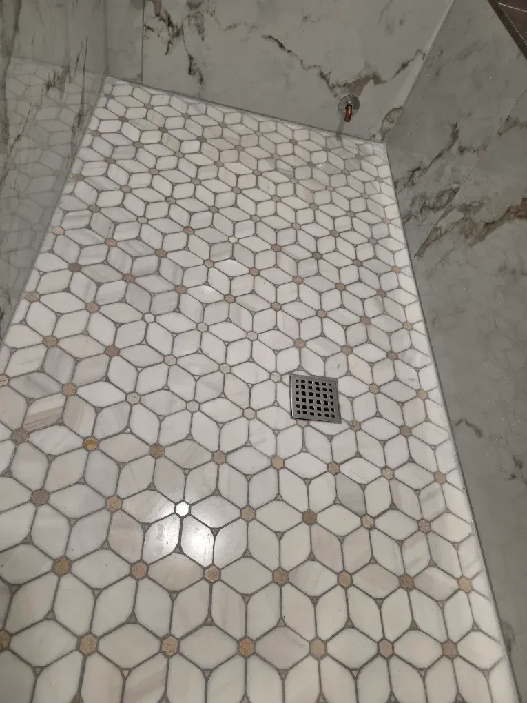 Tiled bathroom shower floor with a drain and light-colored hexagonal tile pattern