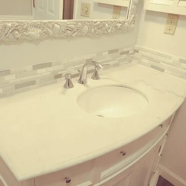 White bathroom vanity with marble countertop, oval sink, chrome faucet, and ornate mirror backsplash.