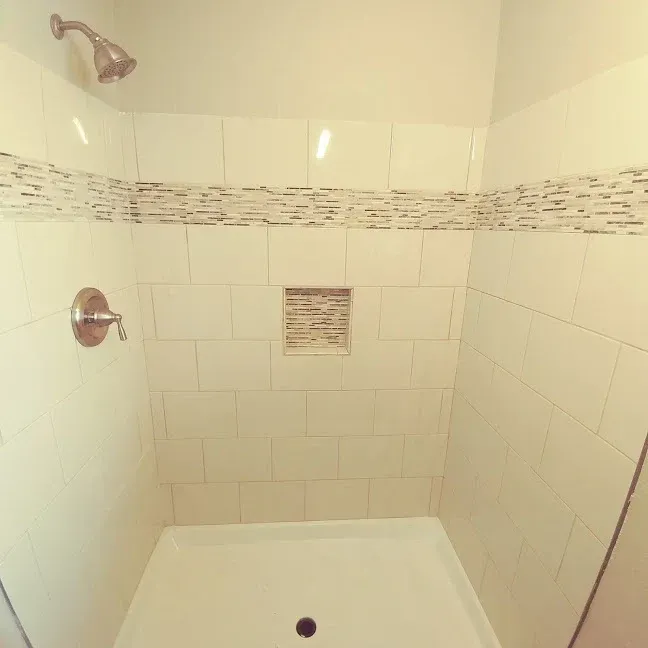 Empty white bathtub and shower with chrome fixtures in a tiled bathroom.