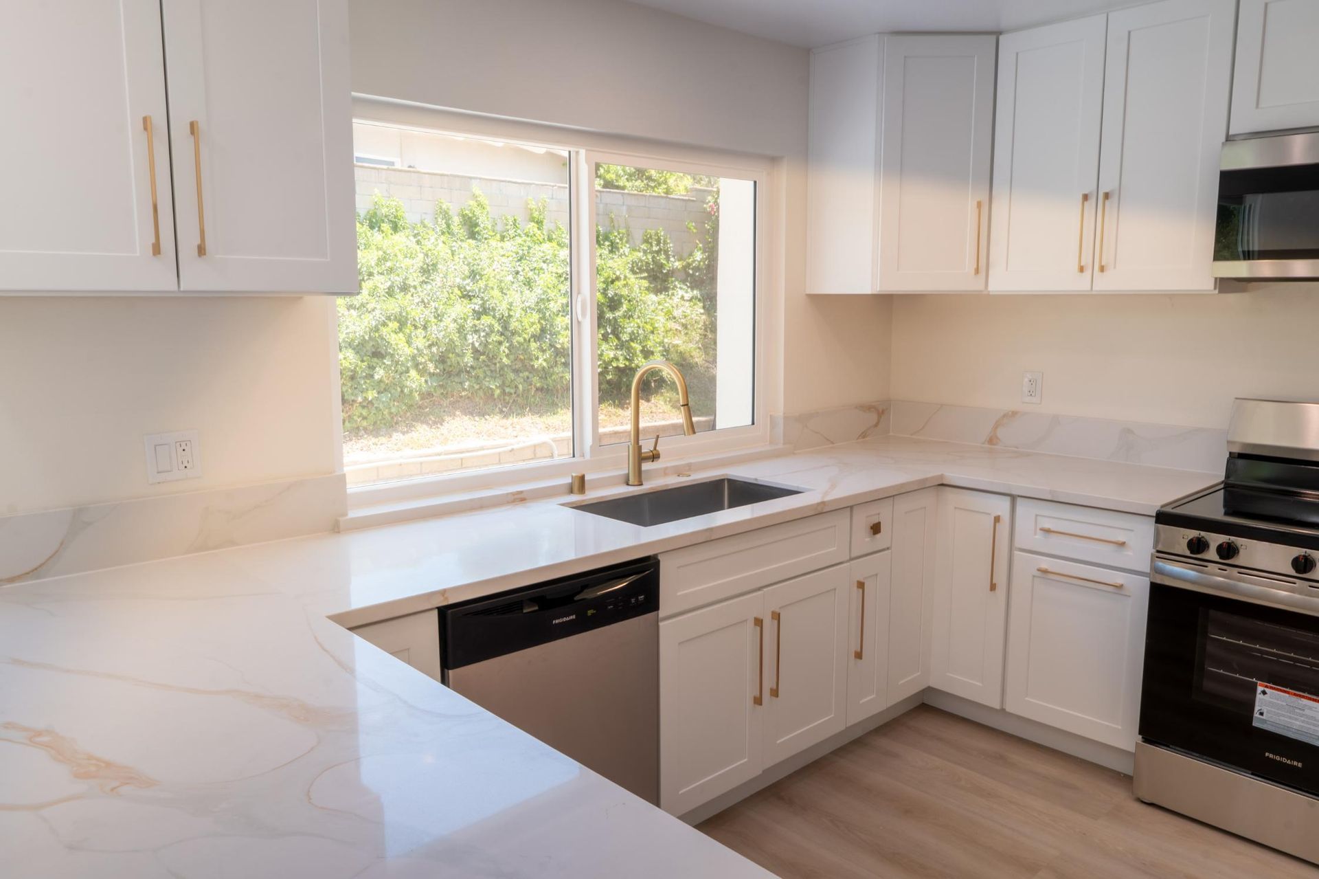 Bright white kitchen with marble counters, stainless stove, and a window over the sink.