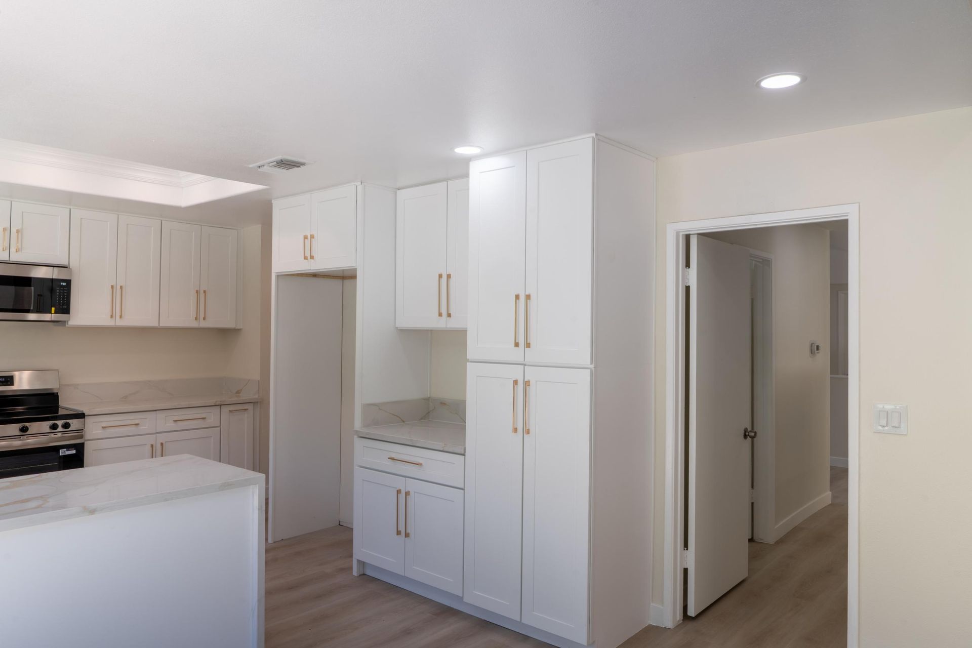 Bright white kitchen with cabinets, marble countertops, and an open doorway to a hallway