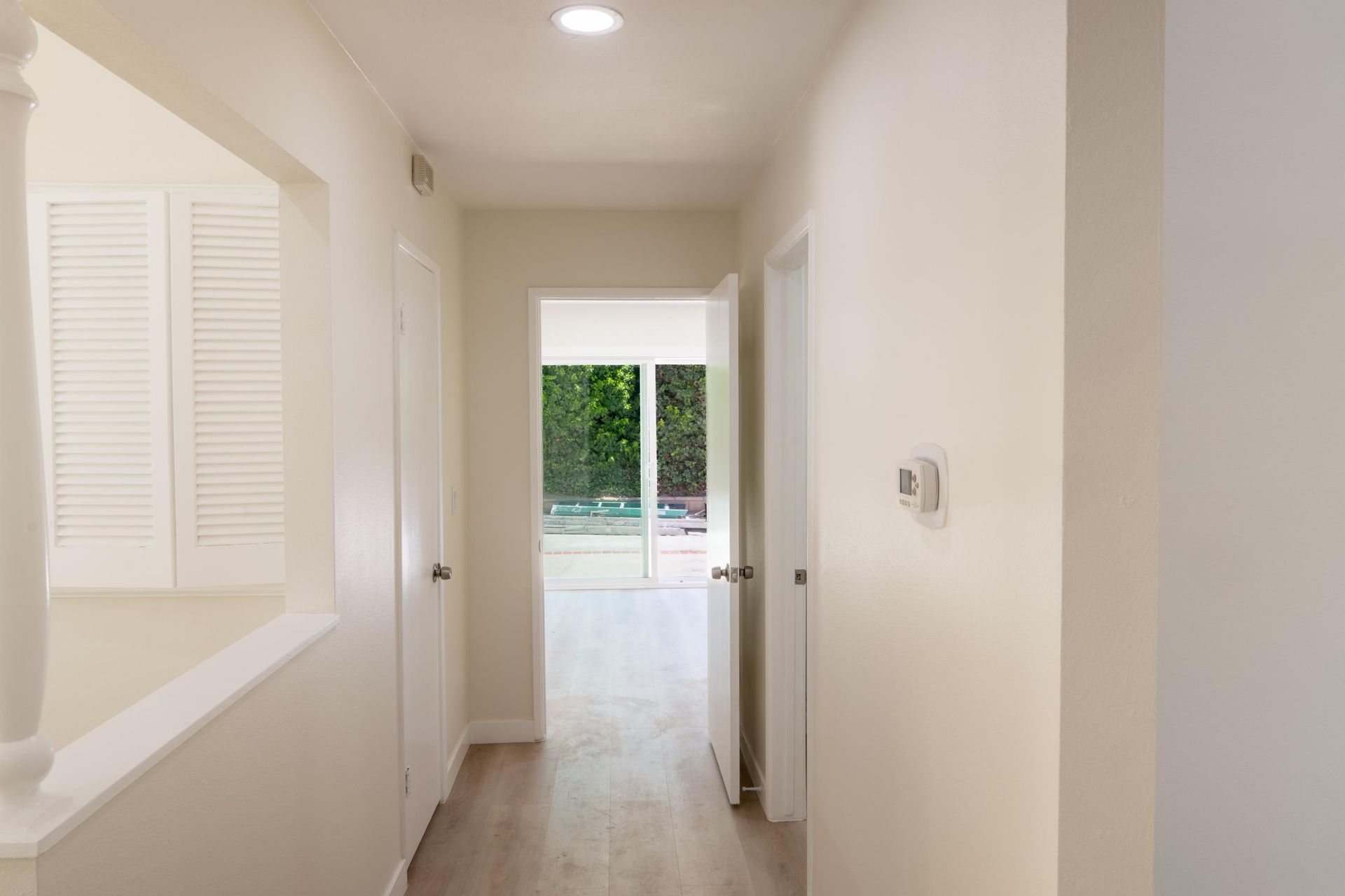 Narrow white hallway with a louvered closet and a bright doorway to a pool outside