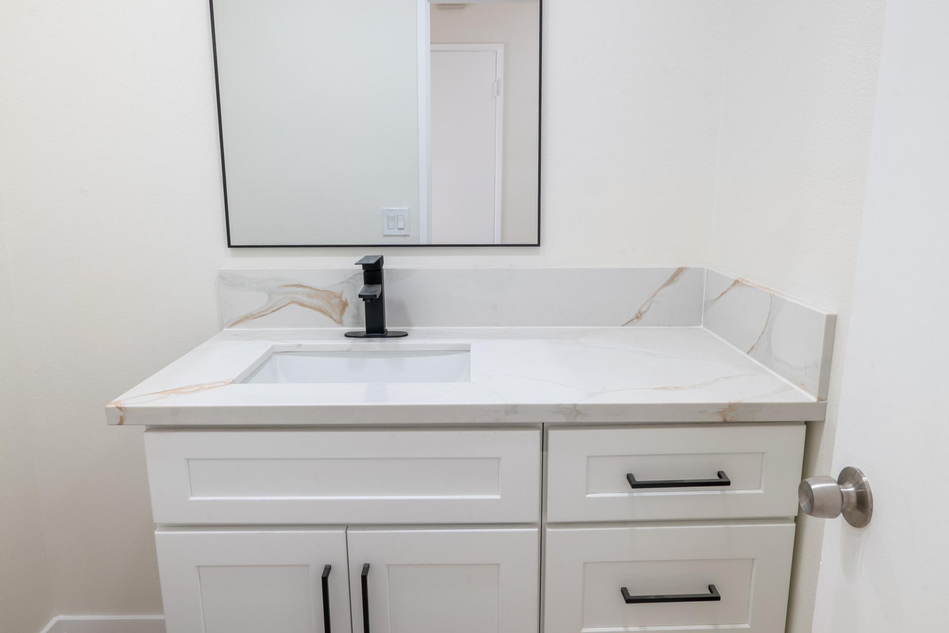 White bathroom vanity with sink, mirror, and chrome faucet beside a closed door