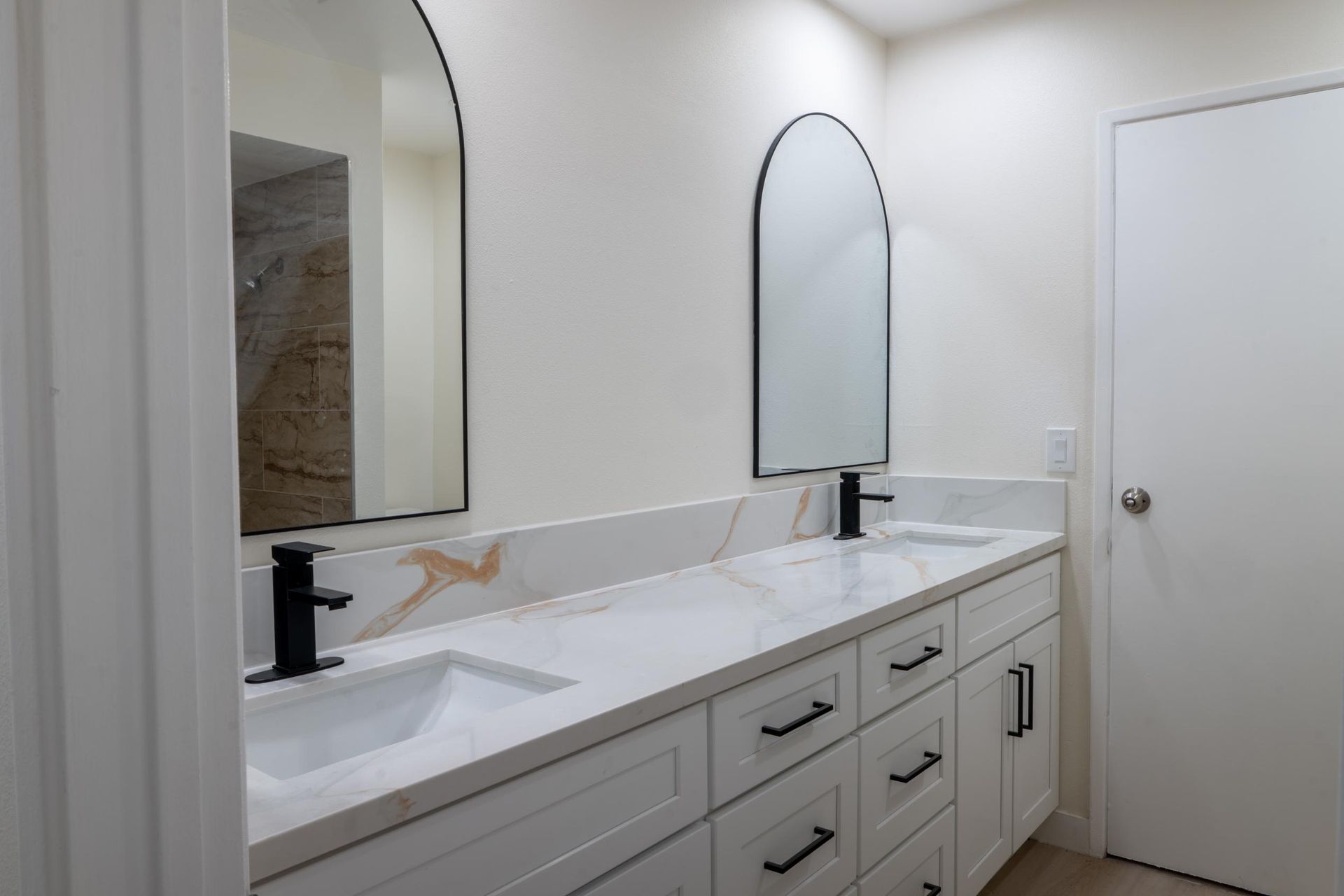 Modern white bathroom vanity with two sinks, black faucets, and arched mirrors