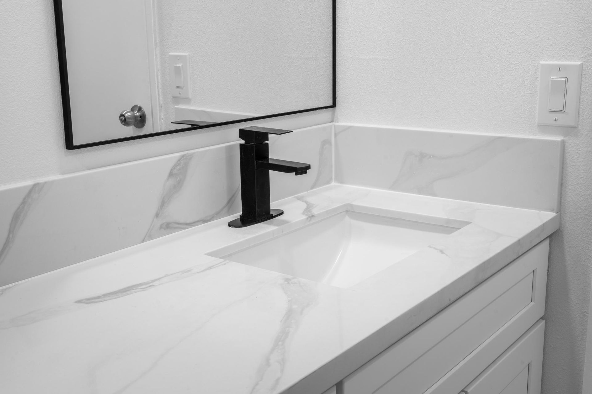 Modern bathroom sink with white countertop, black faucet, and mirror above it