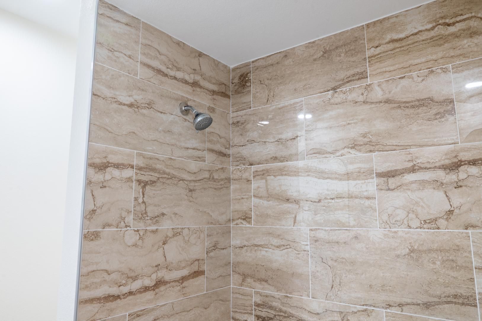 Beige tiled shower corner with a wall-mounted showerhead and white trim