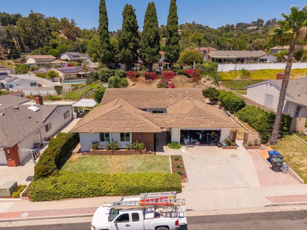 Aerial view of a suburban home with a tiled roof, driveway, and front lawn, with a utility truck parked below