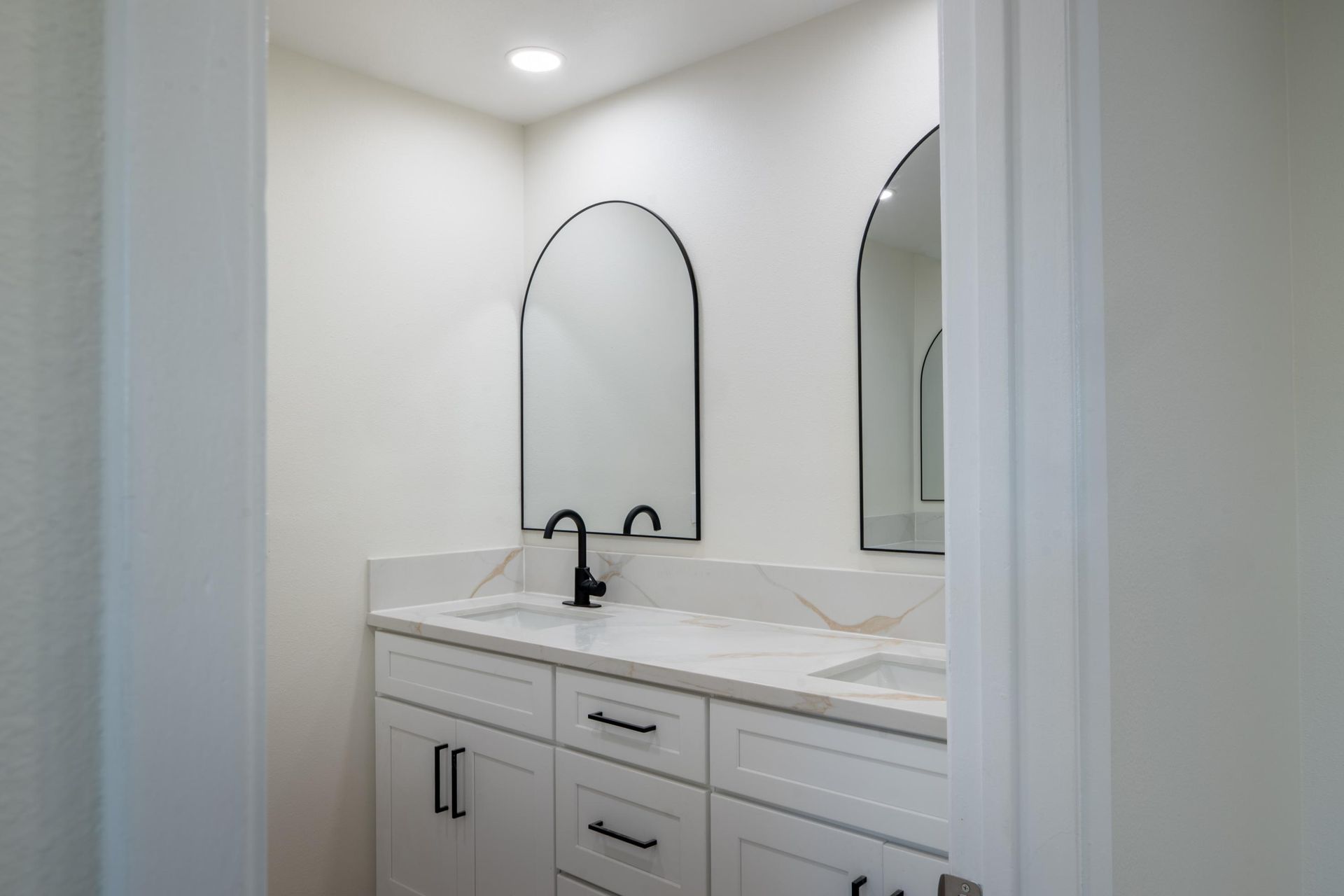 White bathroom vanity with dual arched mirrors and black faucet in a bright, modern interior