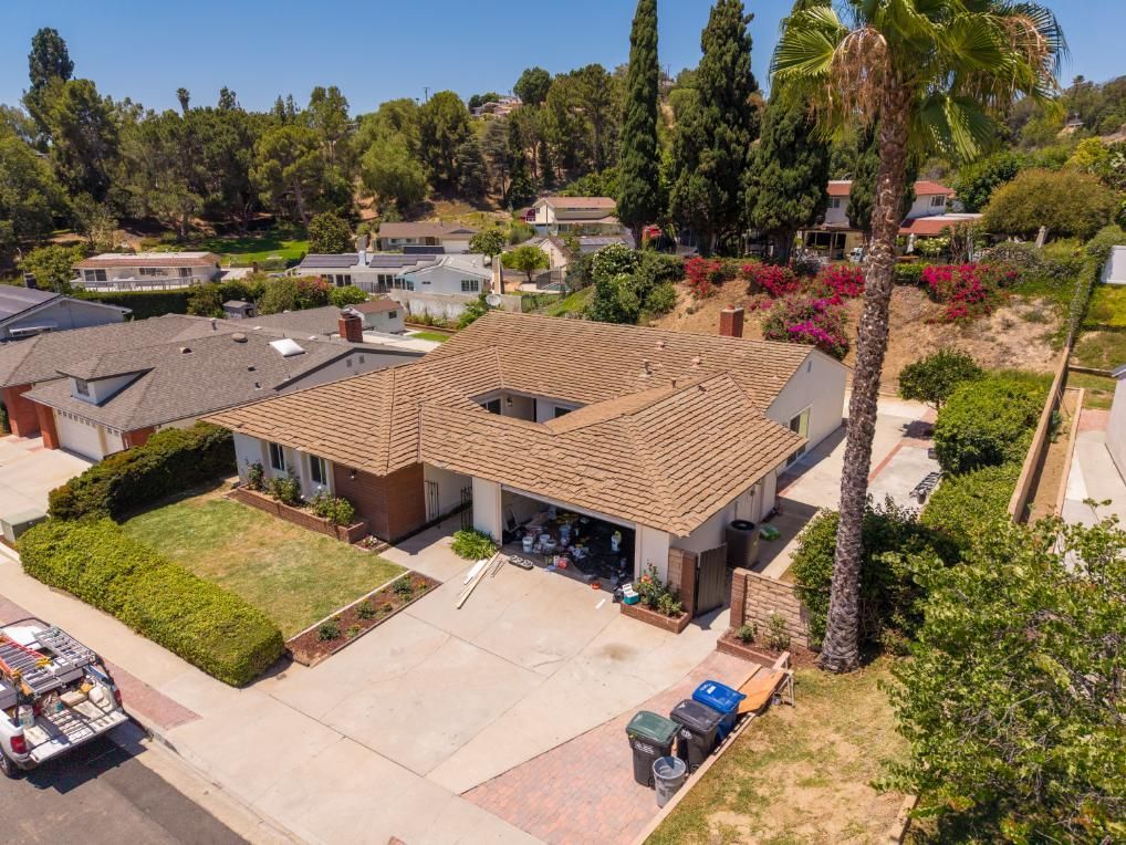 Suburban house with tan roof, driveway, palm trees, and a parked car on a sunny day