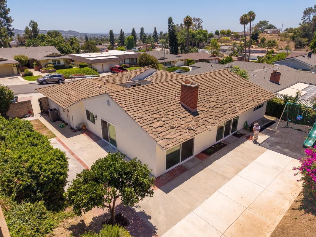 Aerial view of a white house with a tan tile roof and driveway in a suburban neighborhood.