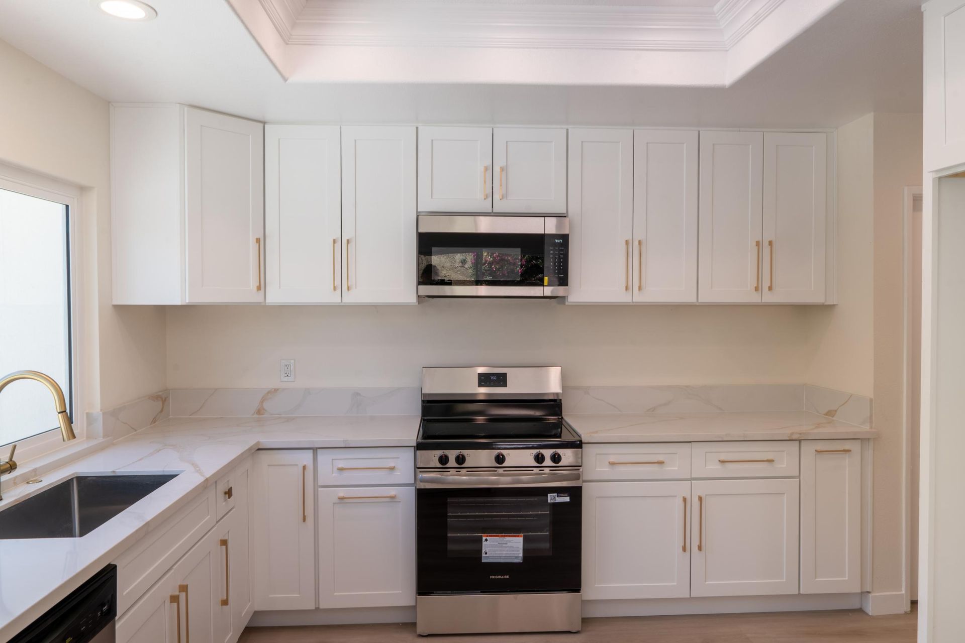 Bright white kitchen with cabinets, stainless stove, microwave, and sink by a window