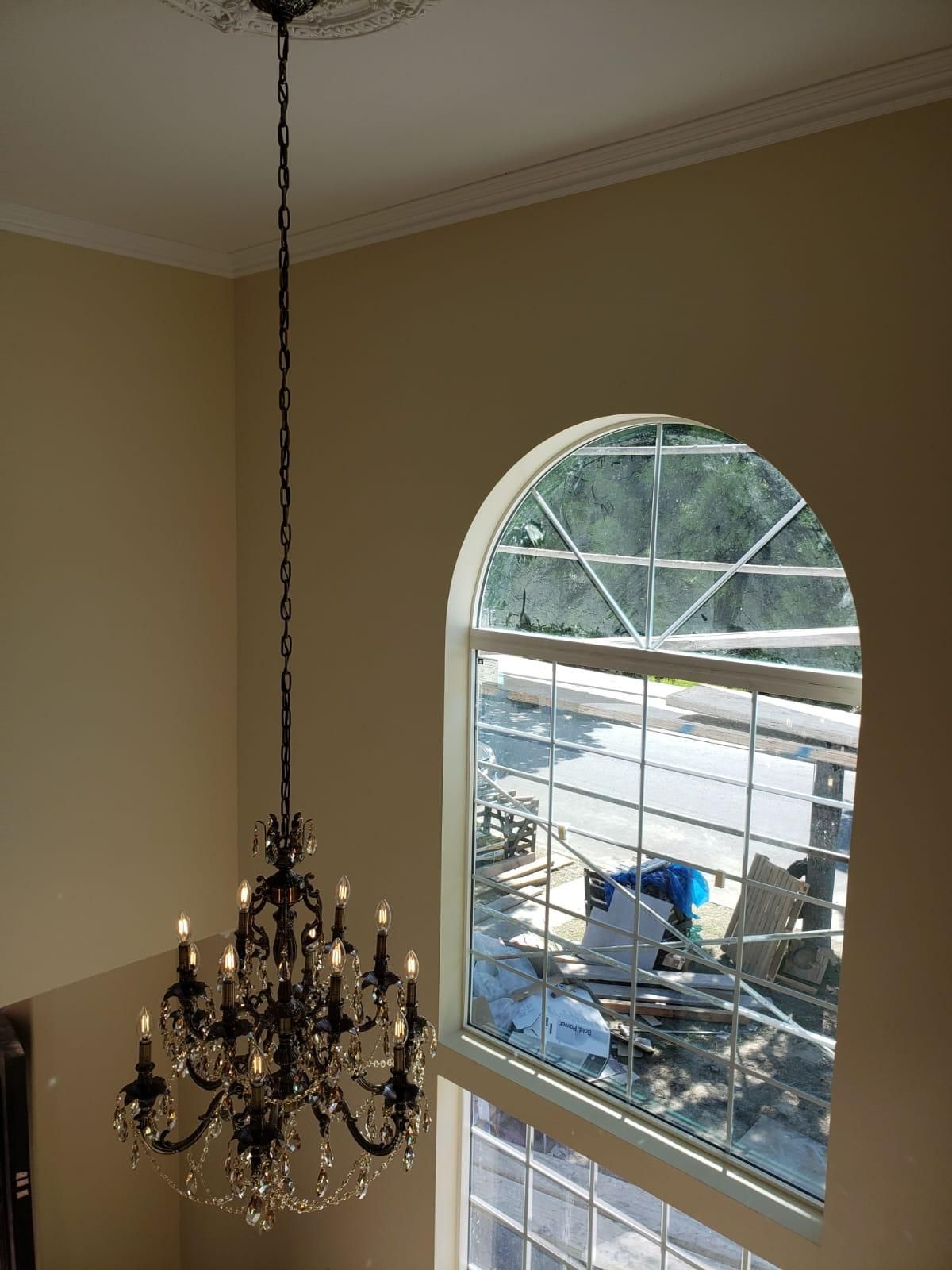 Chandelier hanging in a beige room beside an arched window overlooking a snowy outdoor area.