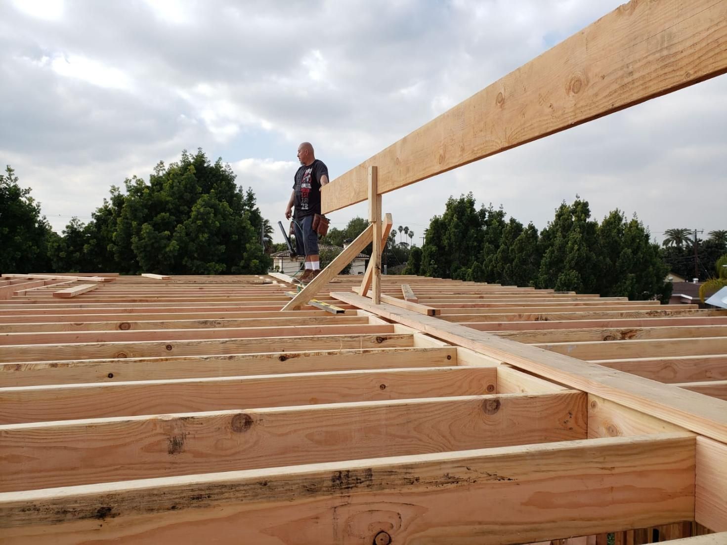Worker standing on roof frame with raised wooden beam under cloudy sky