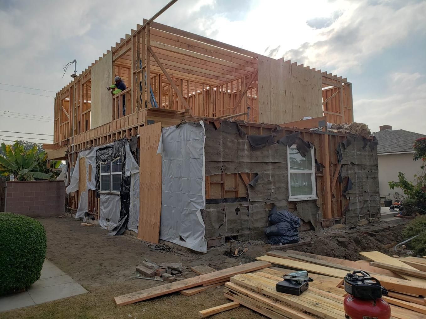 Partially built house with exposed wooden framing and tarps around the lower walls in a residential yard
