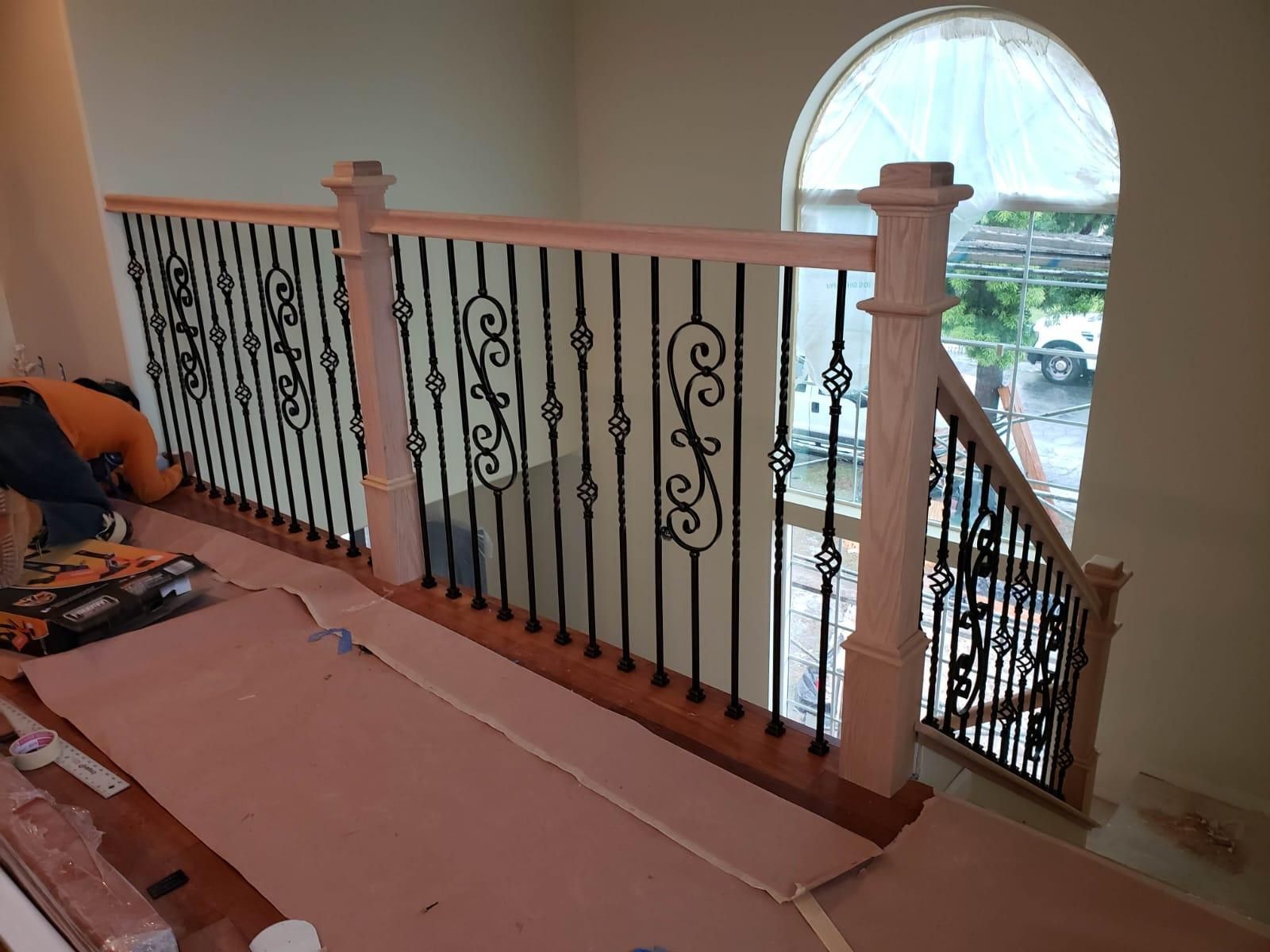 Indoor balcony railing with decorative iron balusters and a large arched window overlooking outside