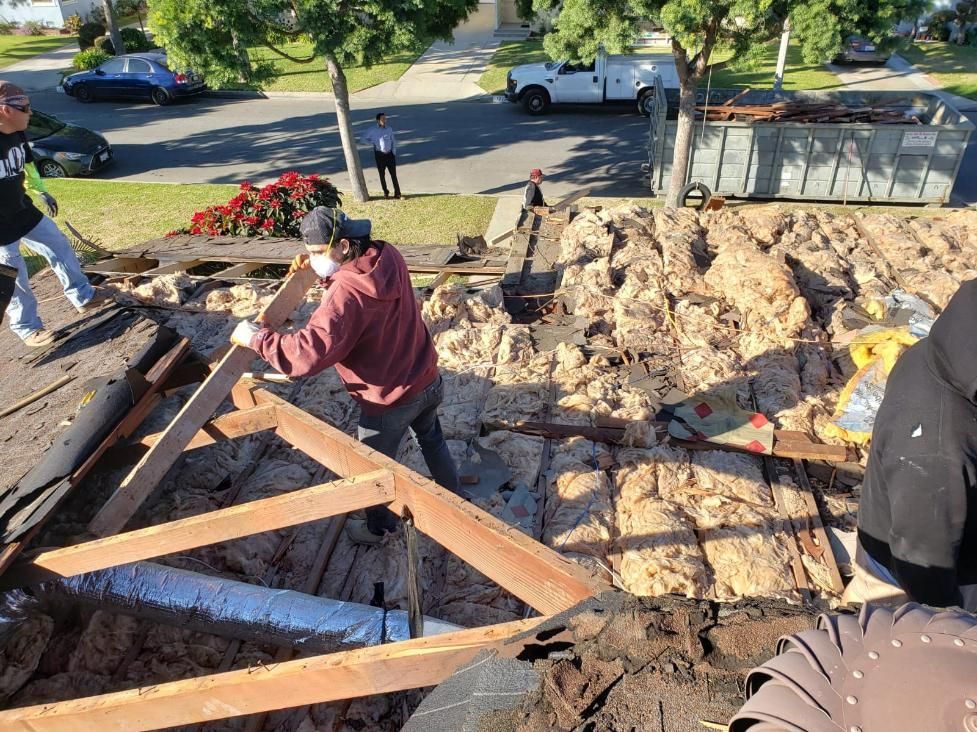 Workers repairing a roof, installing plywood and beams on a sunny residential house