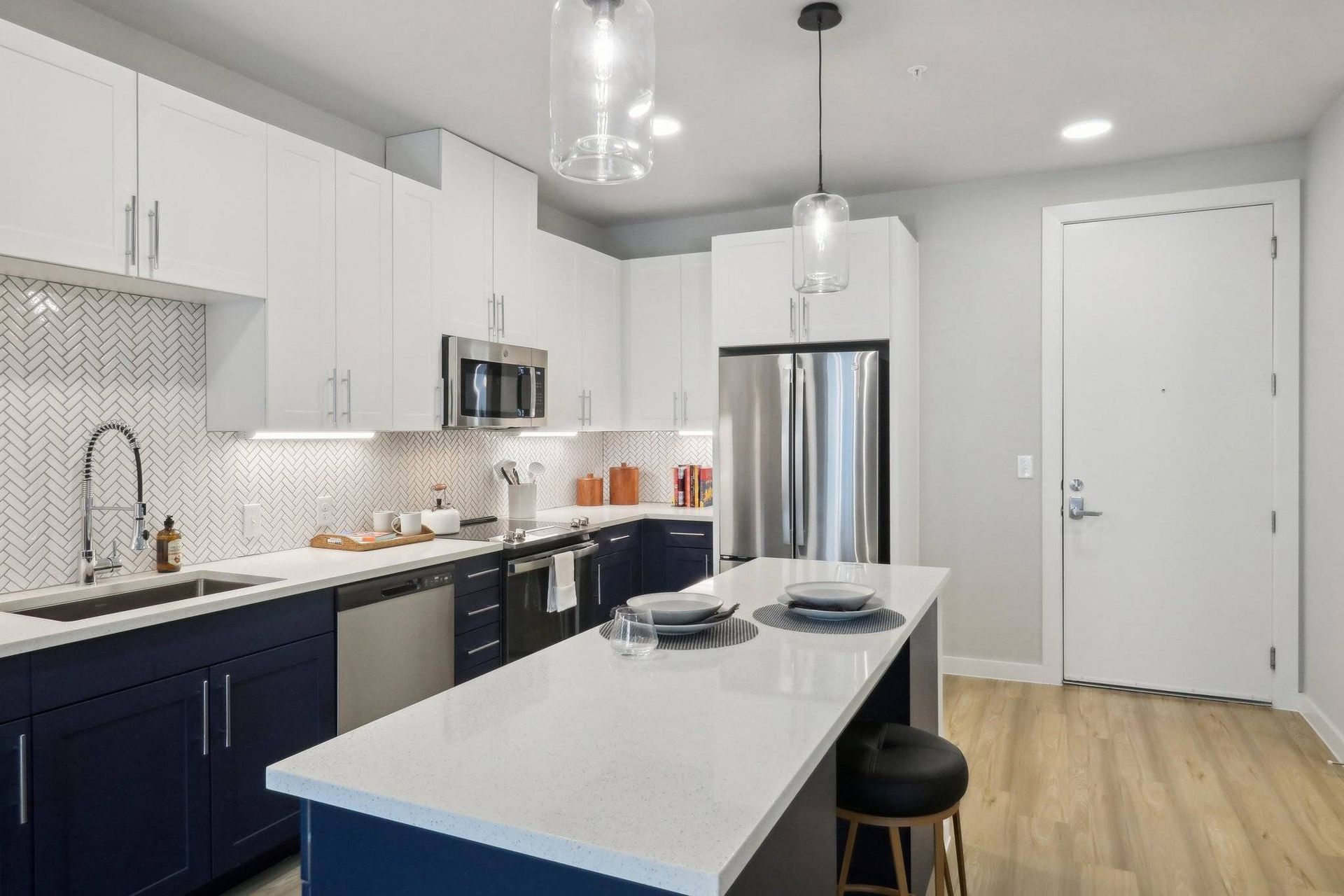 Modern kitchen with white upper cabinets, navy lower cabinets, island, and stainless appliances.