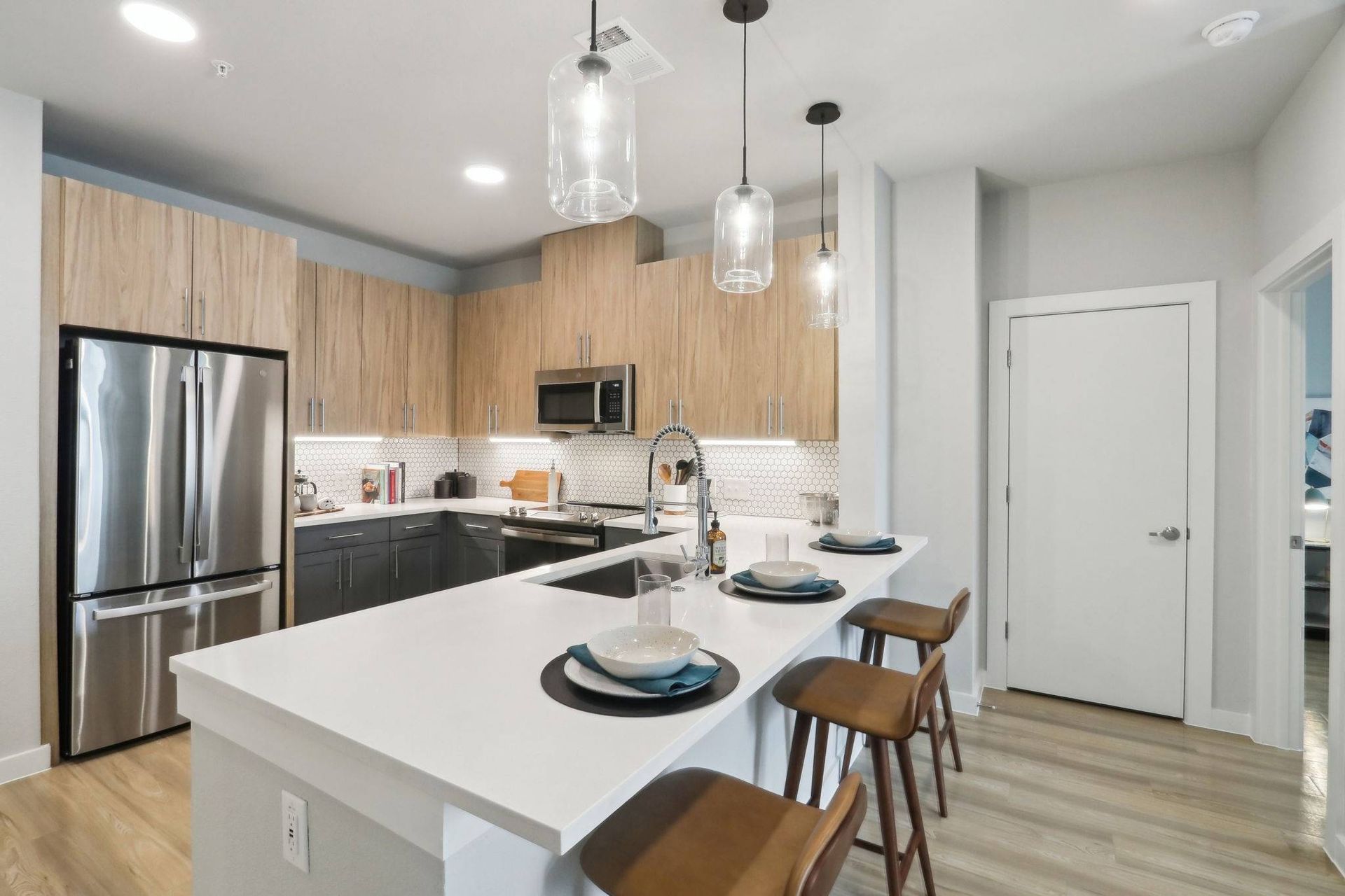 Open-concept kitchen with white island, wooden upper cabinets, and stainless steel appliances.