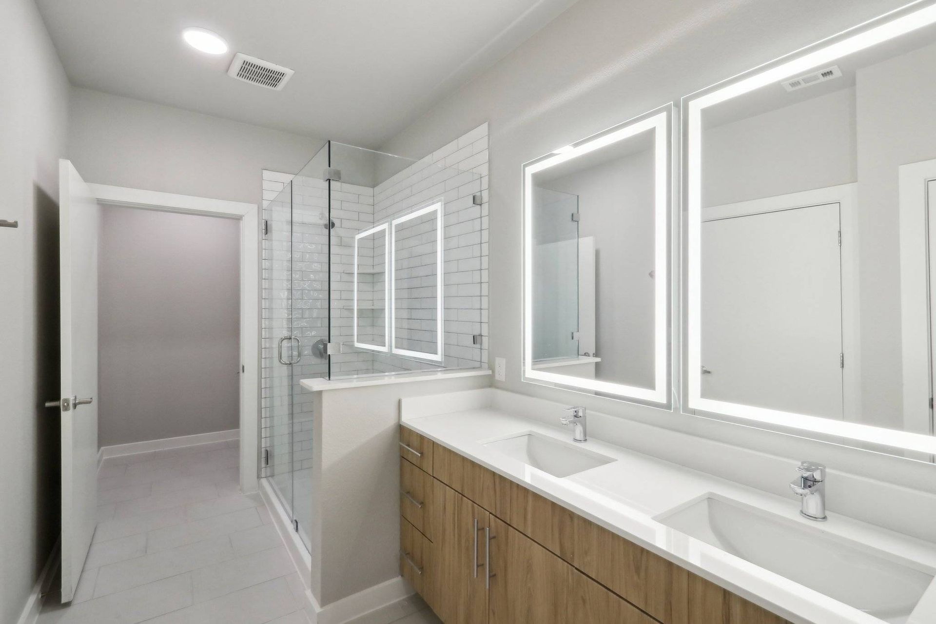 Modern bathroom with a double-sink vanity, glass-enclosed shower, and LED-lit mirrors.