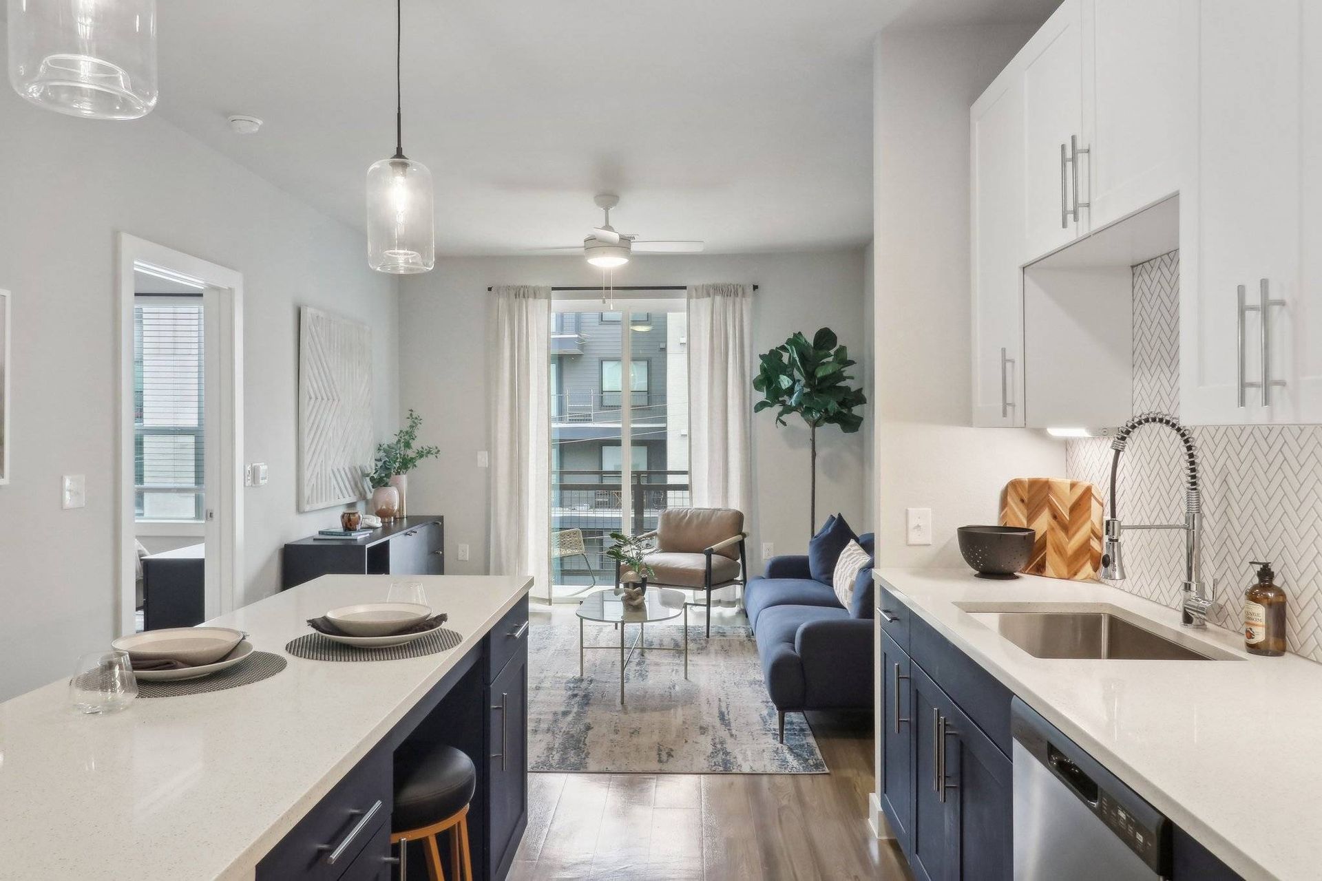 Open-concept kitchen and living area with white countertops, blue cabinets, and a balcony door.