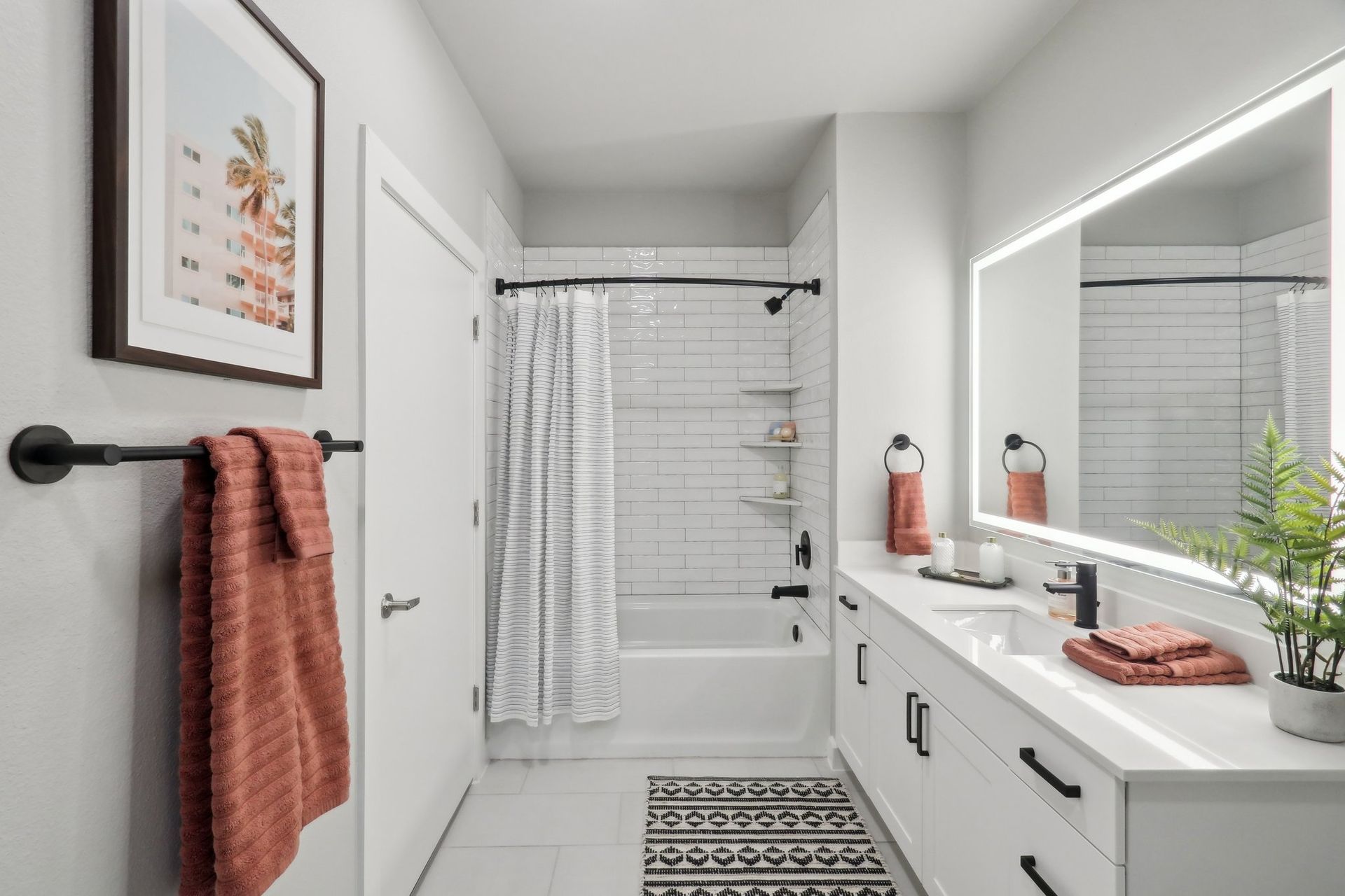 Modern bathroom with white cabinets, large mirror with LED, coral towels, and black accents.