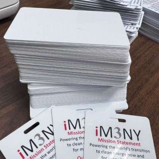 Stack of blank white plastic ID cards on a wooden table, with several iM3NY cards in front