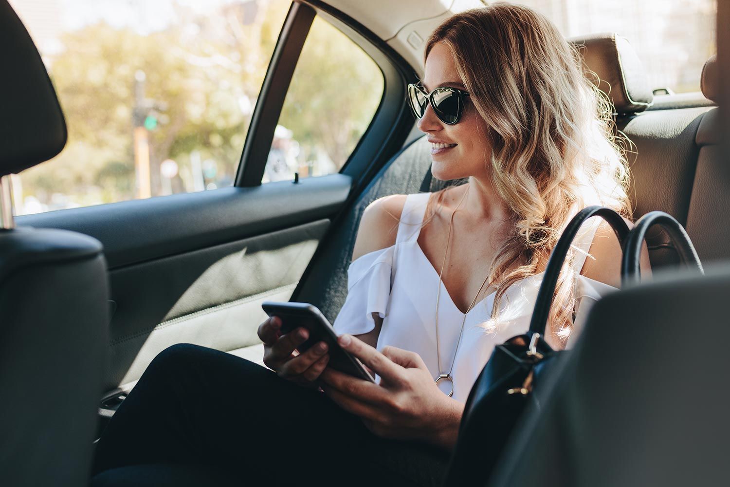 A Woman is Sitting in the Back Seat of a Car Looking at Her Cell Phone — Territory Limousine Service in Marrara, NT