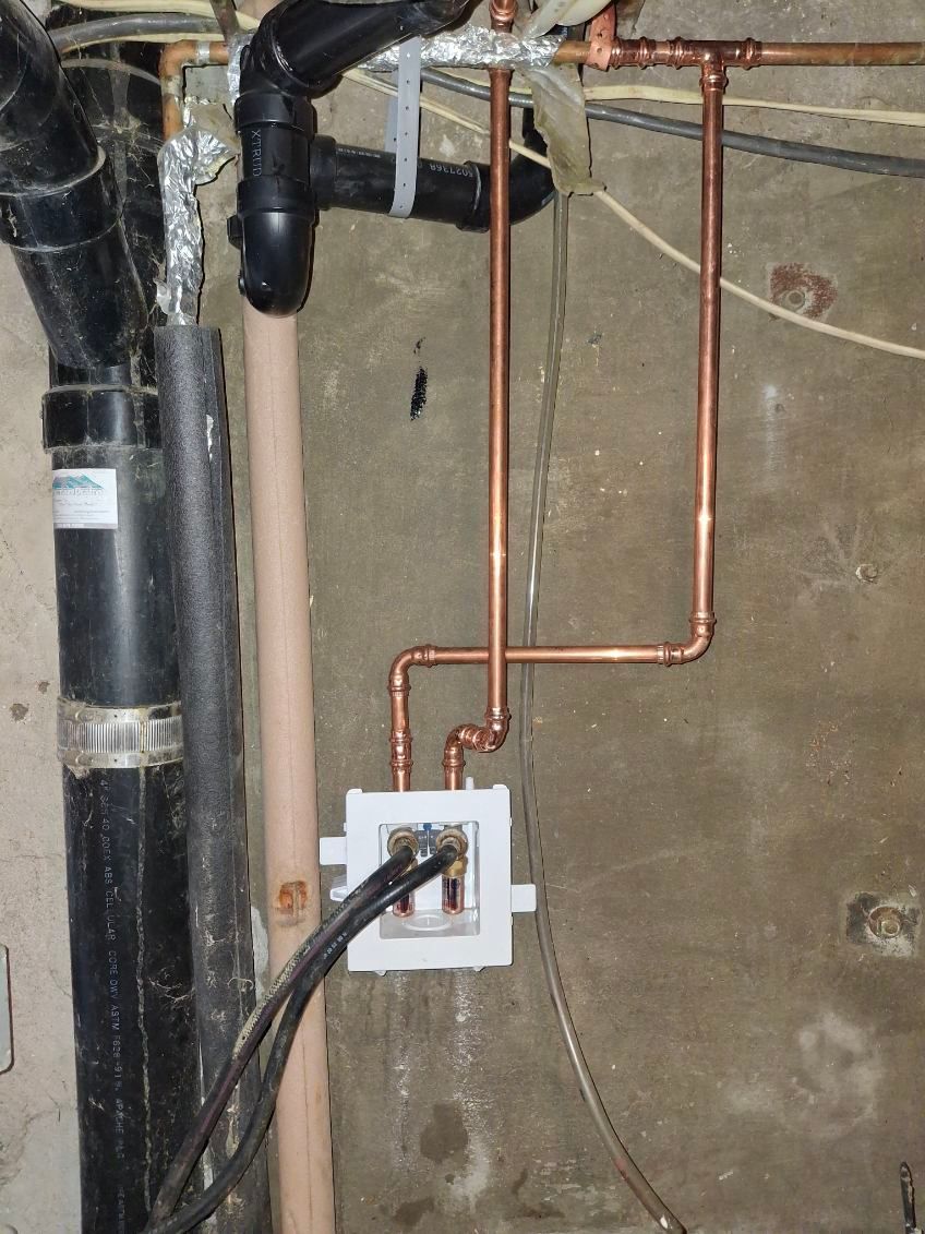 Copper pipes and black utility lines on a concrete basement wall near an electrical box.
