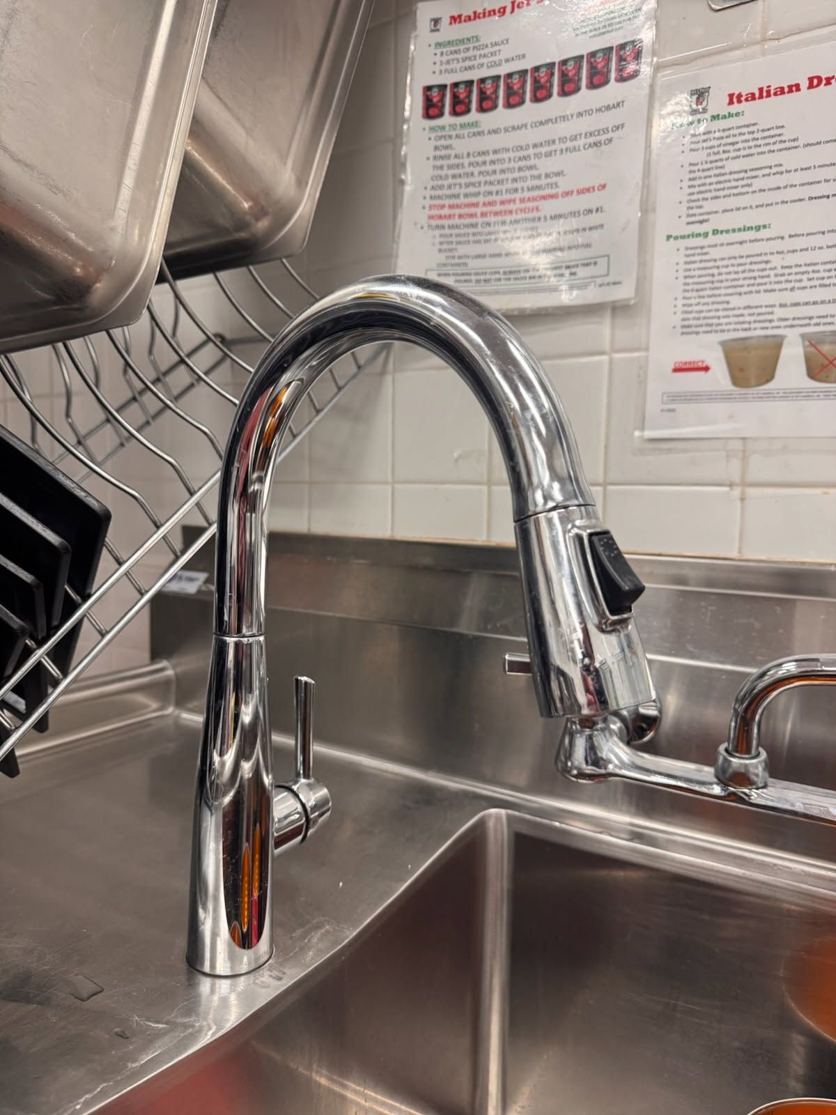 Stainless steel sink with chrome pull-down faucet in a commercial kitchen or prep area.