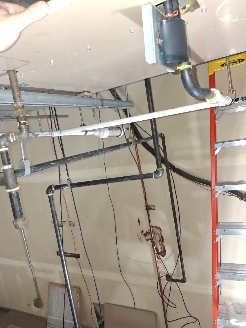 Exposed plumbing and pipes in a basement ceiling with a red ladder at right