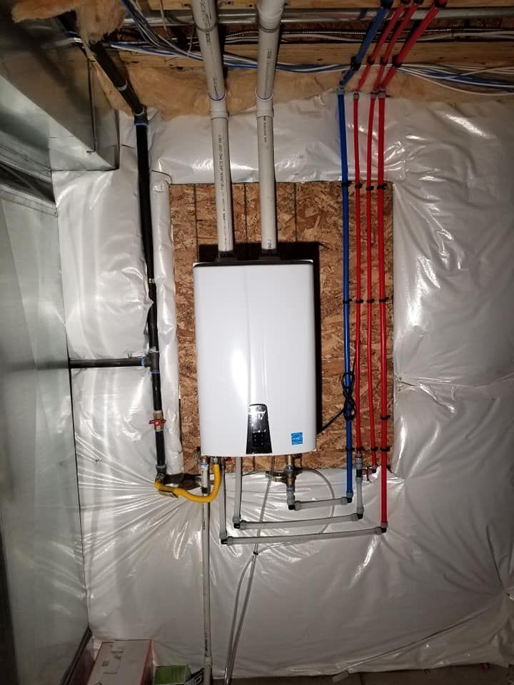 Water heater mounted in an insulated utility room, with exposed pipes and electrical wiring.