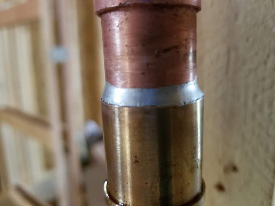 Close-up of a copper pipe joint with a brass fitting against a beige wall