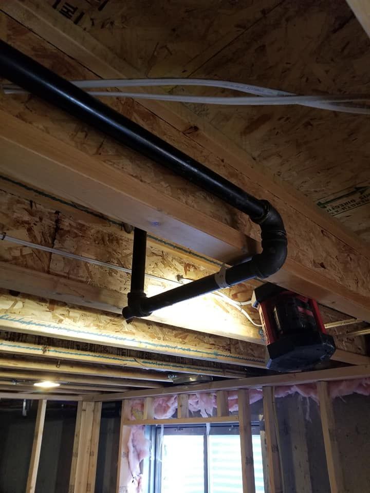 Exposed attic framing with black ventilation ducting and a bright work light near a window opening