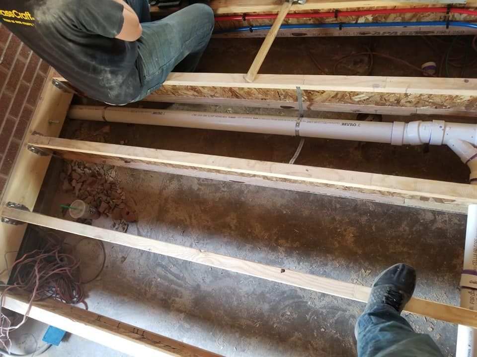 Exposed floor joists and plumbing with two people working in a crawlspace or renovation area
