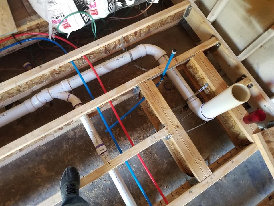 Exposed floor joists with plumbing pipes and red and blue wiring in a renovation area