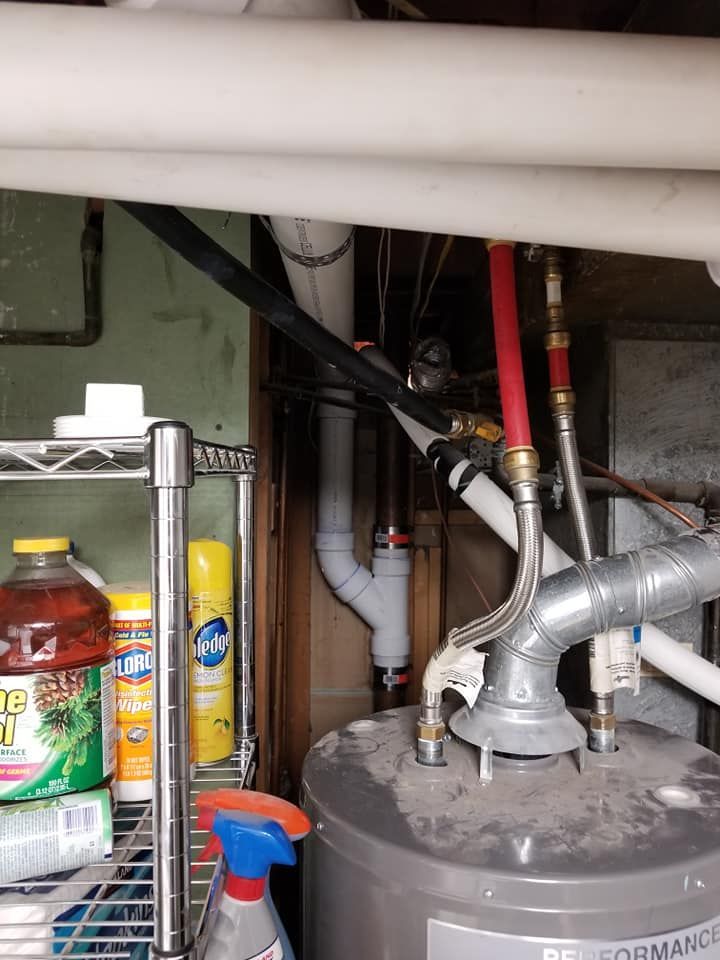 Under-sink utility area with pipes, water heater, cleaning supplies, and a storage shelf