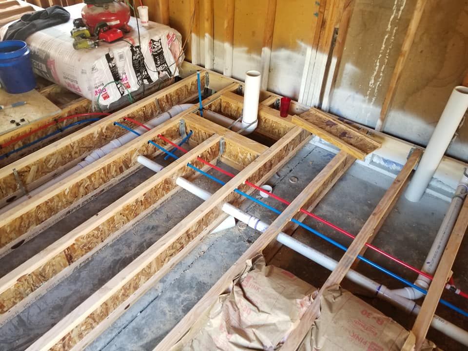 Exposed floor joists with red and blue pipes and insulation in a room under construction