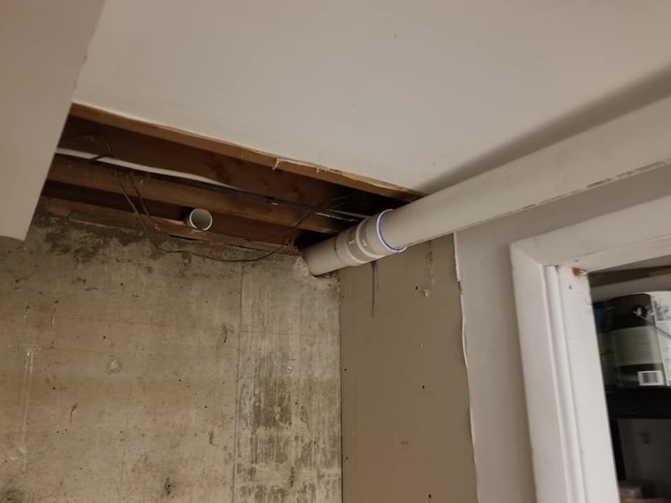 Exposed ceiling joists and ductwork above a bare concrete wall in an unfinished room.