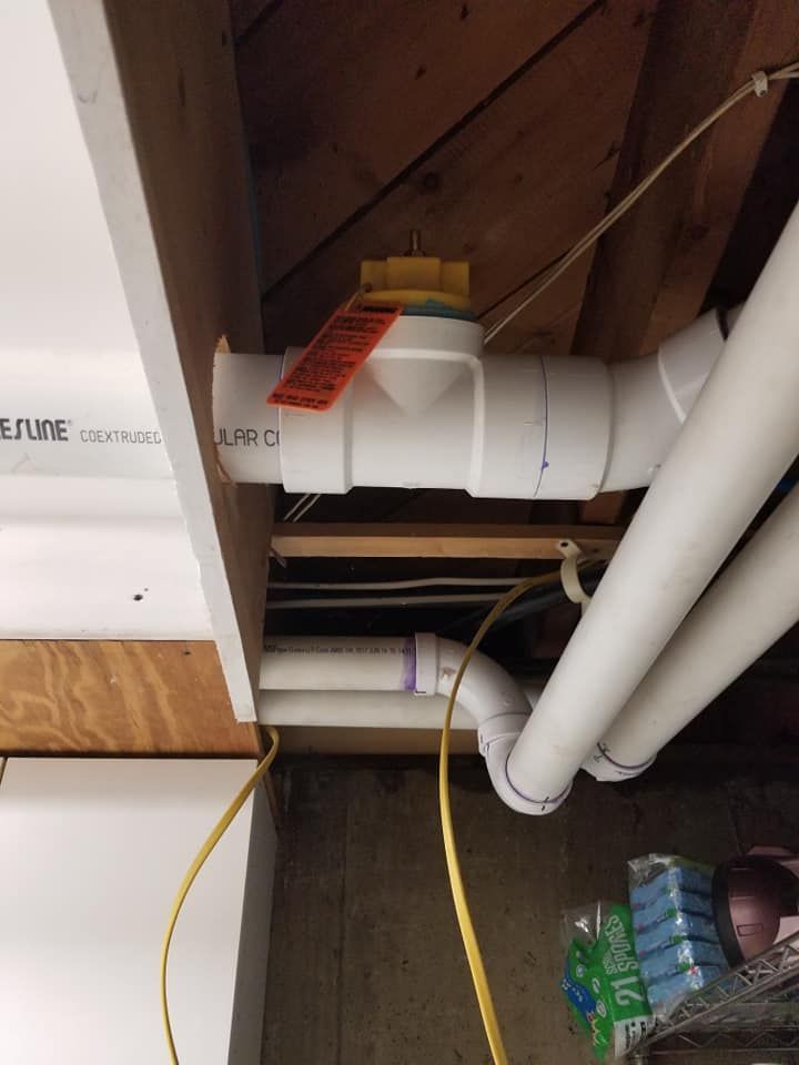White PVC pipes and ceiling beams in a utility space, with a yellow cable and a hand near a pipe joint