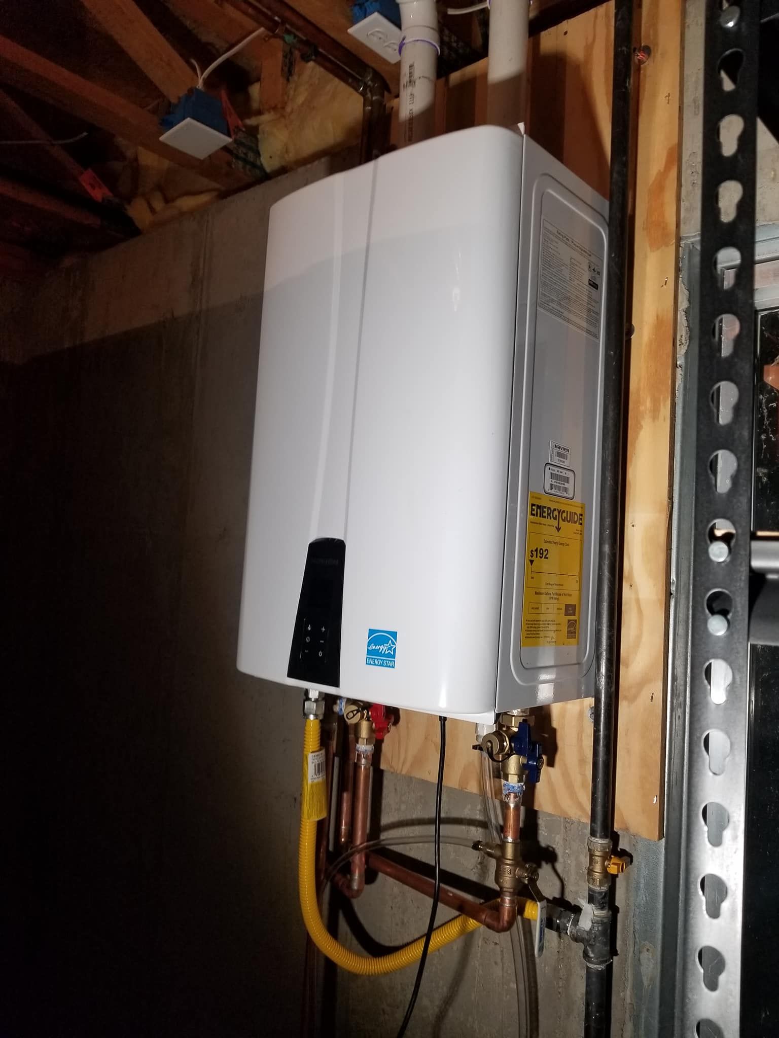 White wall-mounted water heater with pipes and valves in a basement or utility area