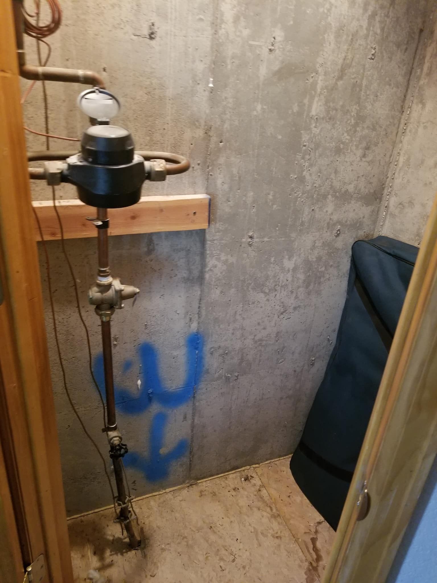 Utility meter and pipes mounted on a concrete wall in a basement corner.