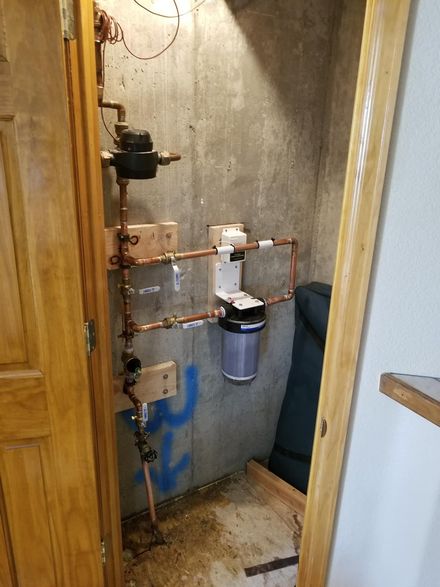 Basement utility area with water softener, pipes, and meters along a concrete wall