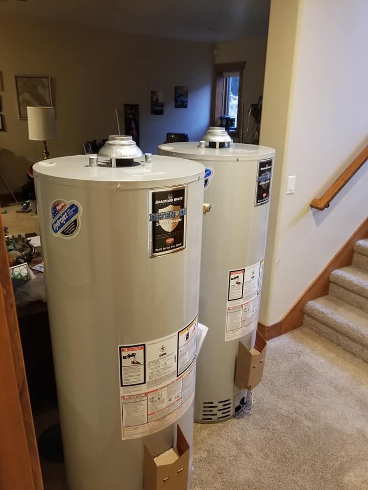Two large beige water heaters in a home hallway beside a staircase.